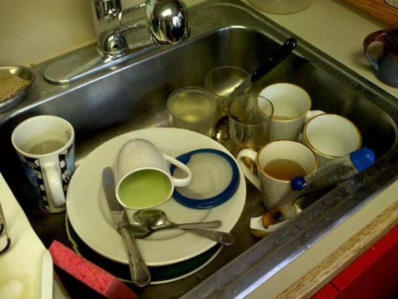 A sink piled high with dirty mugs, plates, and cutlery